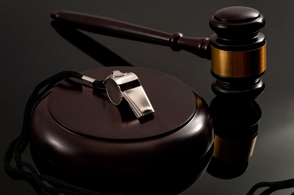 Silver whistle on a lanyard resting on a wooden gavel sound block next to a judge’s gavel